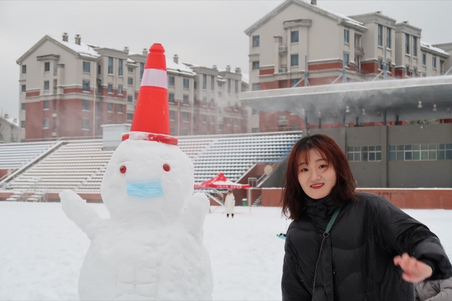 Next to a snowman wearing a traffic cone